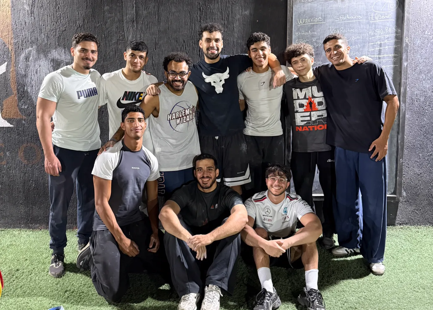 TripleOneBars athletes and coaches together in front of the gym's chalkboard.