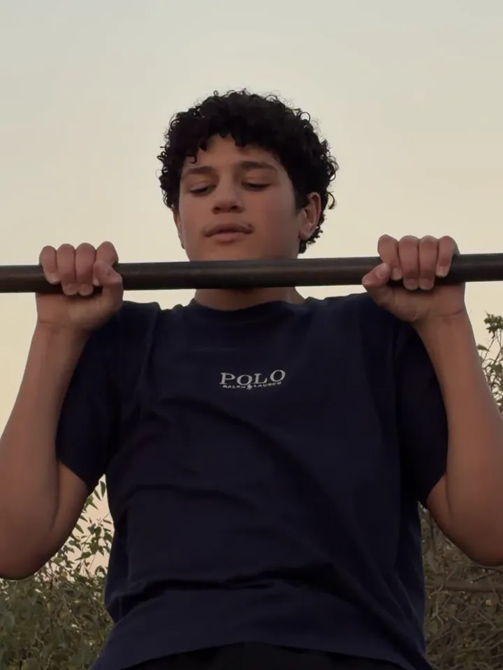 A young athlete pulling his chin over the bar at sunset.