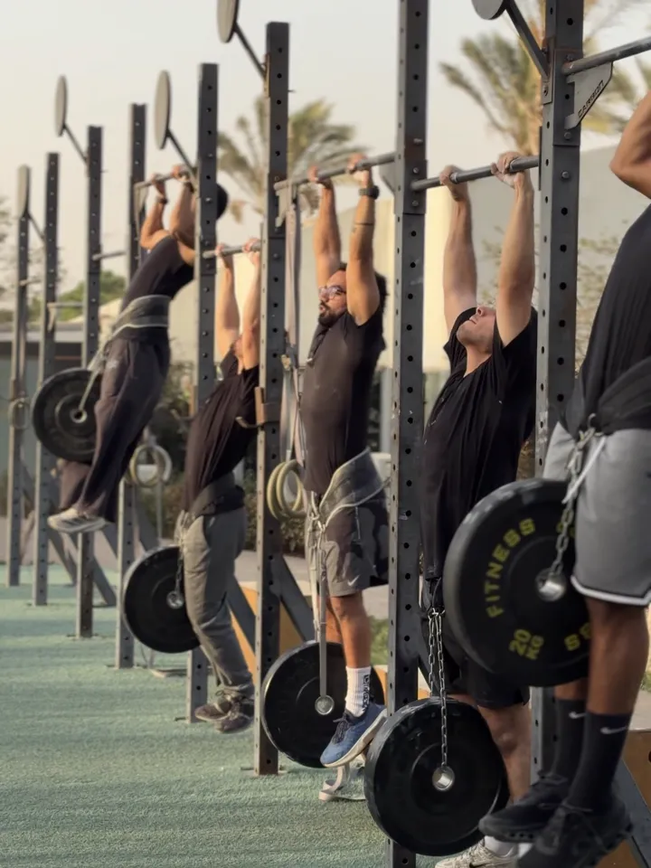 A line of athletes doing pull-ups with weight plates hanging from their belts.